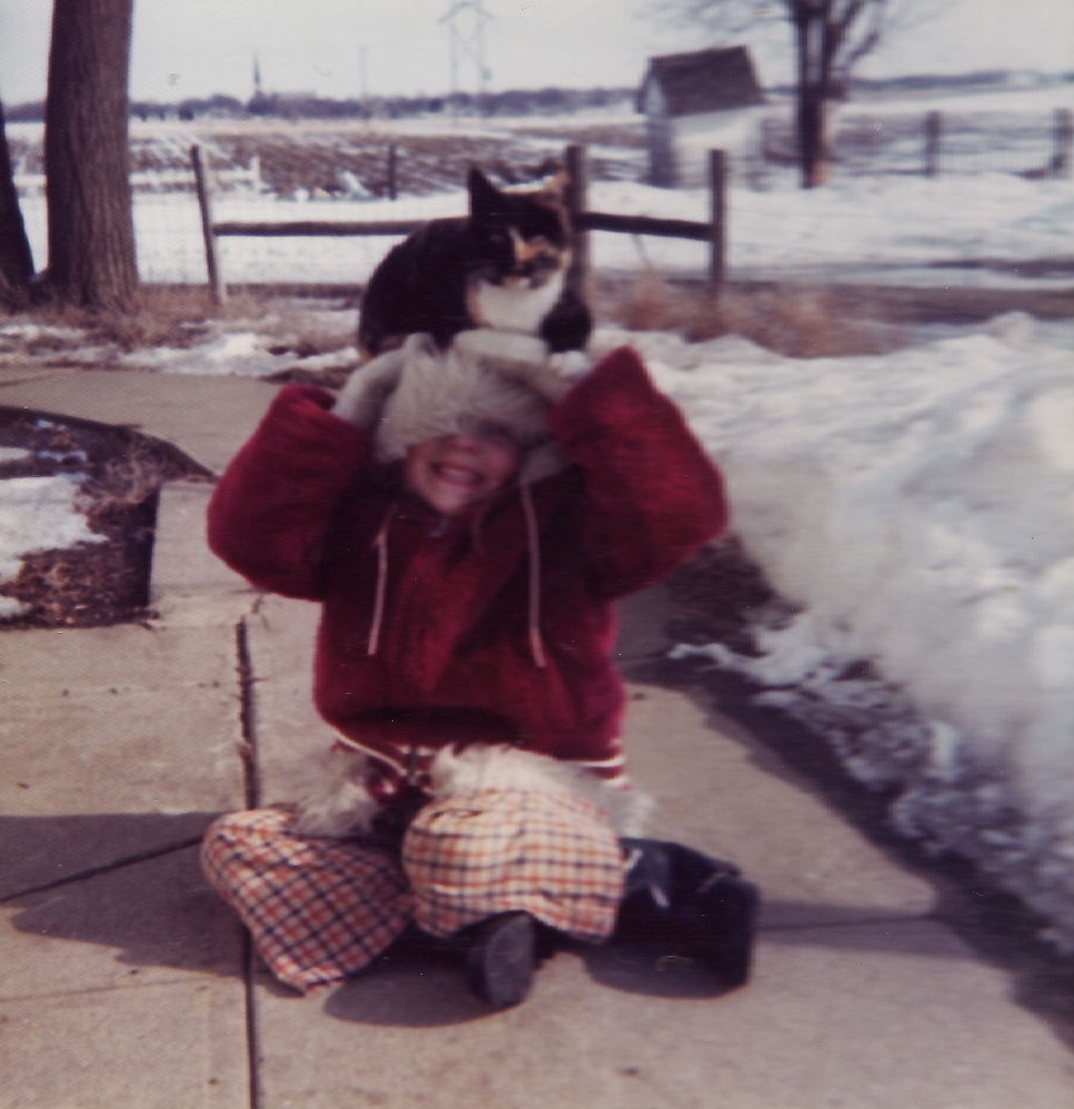 Me, circa 1973, with my cat, Flower. She loved to sit on my head! You can see our outhouse in the background. On a small hog farm outside of Humphrey, Nebraska.